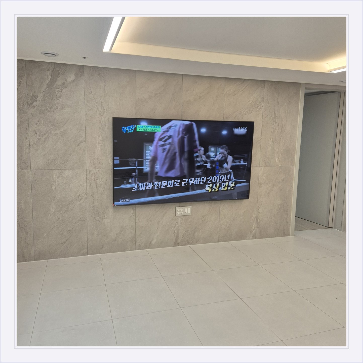 석재 느낌 벽면을 정면에서 본 TV, 벽 마감의 세로 이음선이 TV 양옆에 남아 있습니다