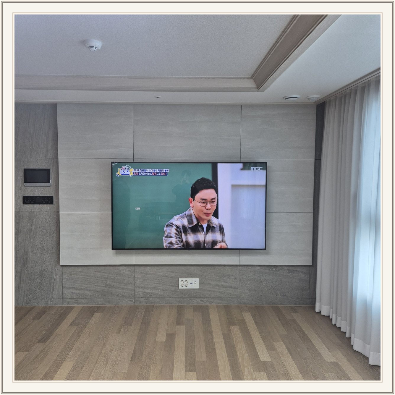 거실 회색 패널과 벽걸이 TV, TV 아래 콘센트와 양쪽 마감 판넬의 대비가 뚜렷합니다