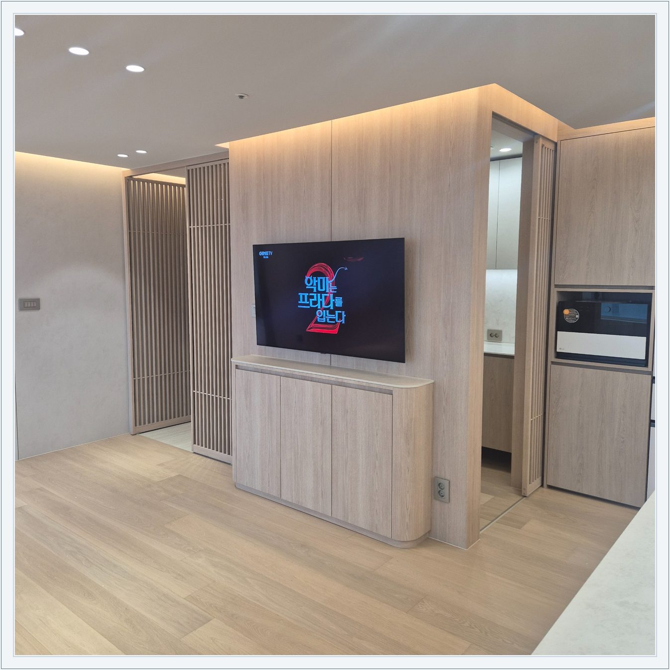 세로 원목 패널 위에 걸린 TV와 수납장, 격자 형태 파티션을 끼고 TV가 놓인 위치를 확인할 수 있습니다