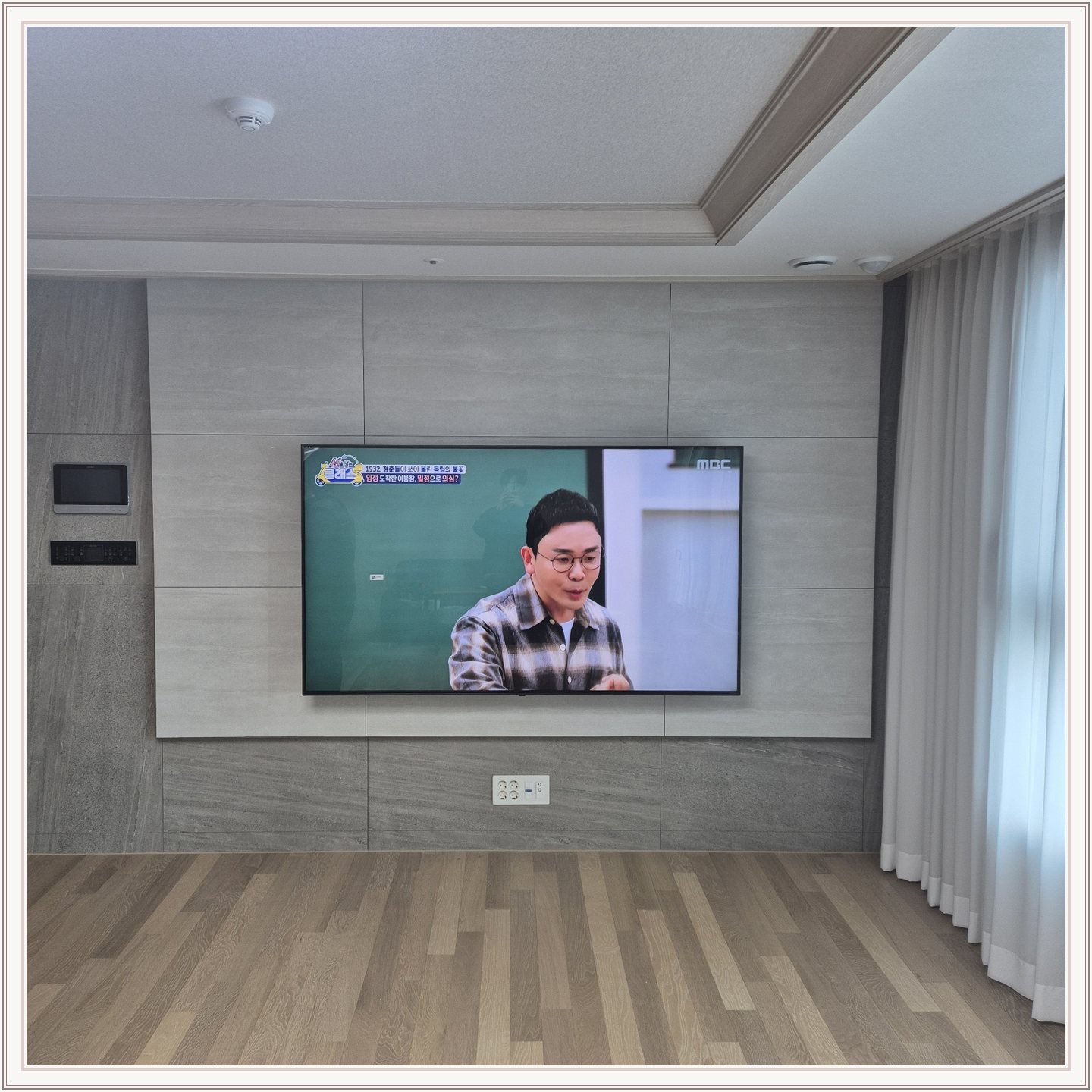 거실 회색 패널과 벽걸이 TV, TV 아래 콘센트와 양쪽 마감 판넬의 대비가 뚜렷합니다